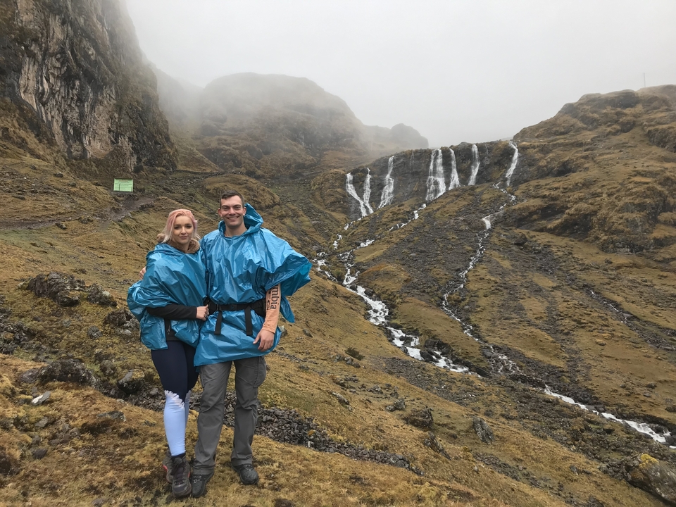Couple en ponchos de pluie debout devant une cascade par une journée brumeuse.