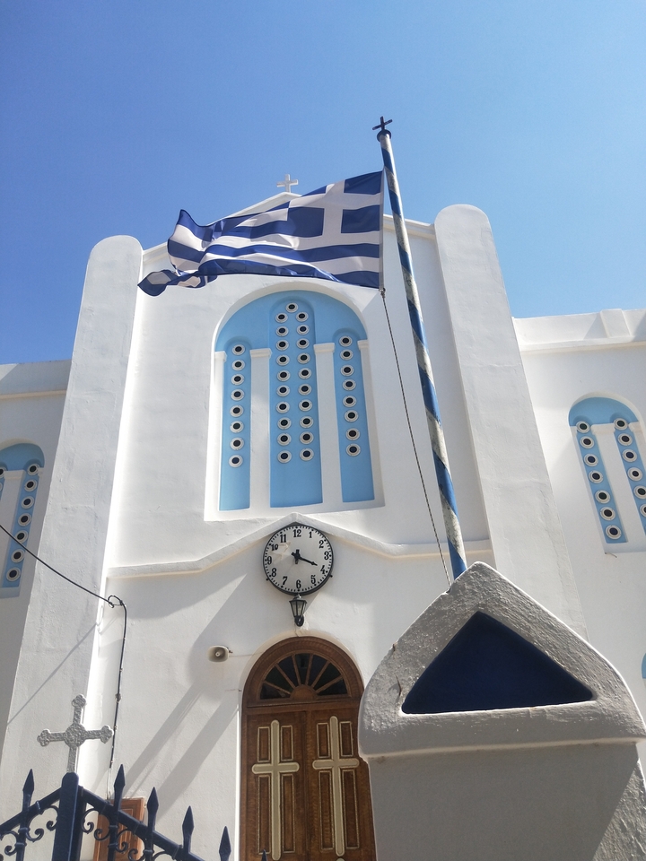 White clock tower with blue accents and a Greek flag.