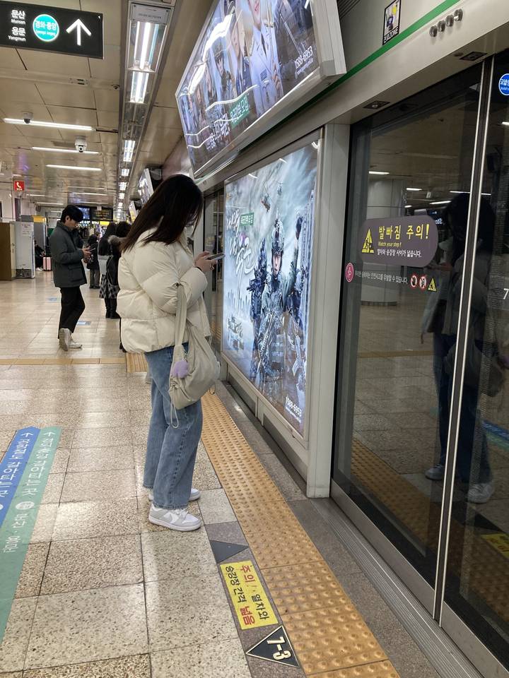 Une femme qui attend sur un quai de métro avec une signalisation coréenne.