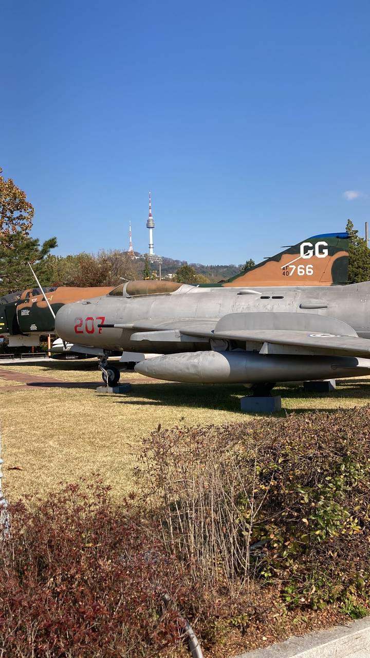 Exposition extérieure d'un avion de chasse militaire avec une tour de communication au loin.