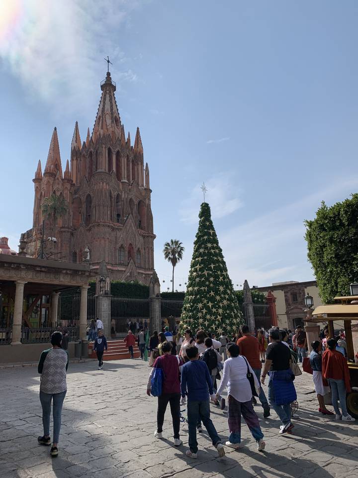 Des gens marchant vers un grand sapin de Noël et une église historique.