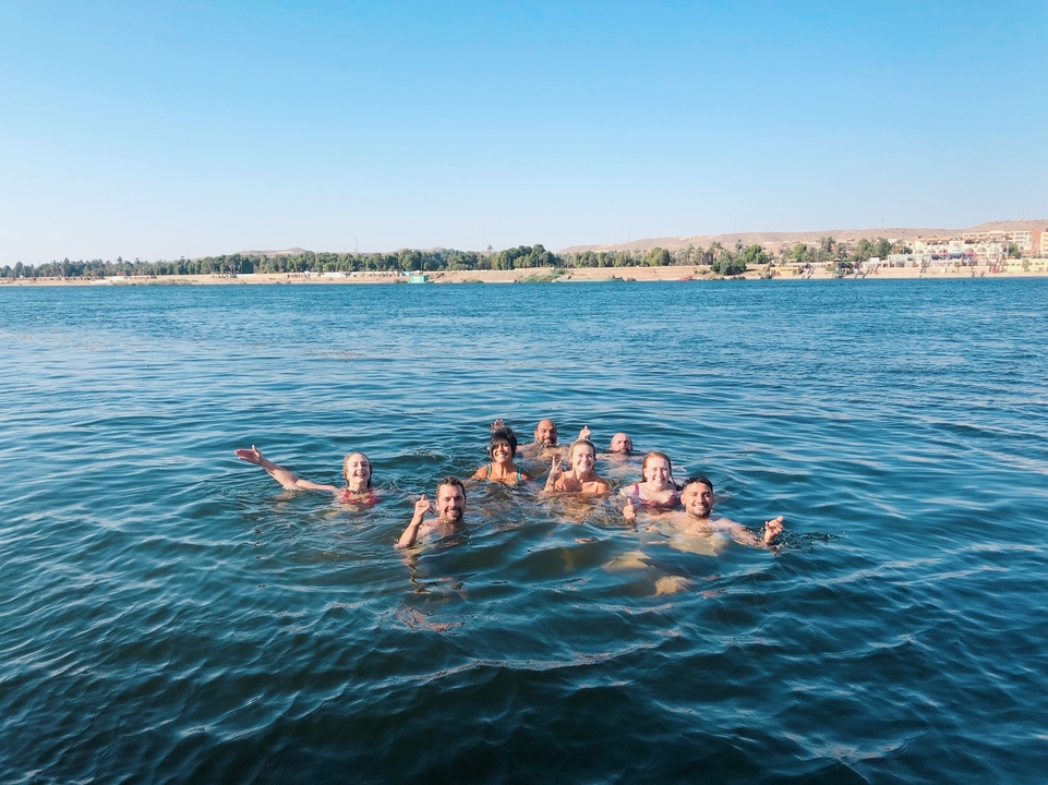 Un groupe de personnes nageant dans une rivière avec une ville en arrière-plan.