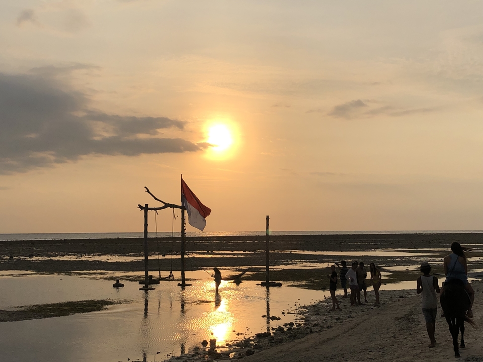 Sunset over the beach with a flag and people silhouetted against the orange sky.