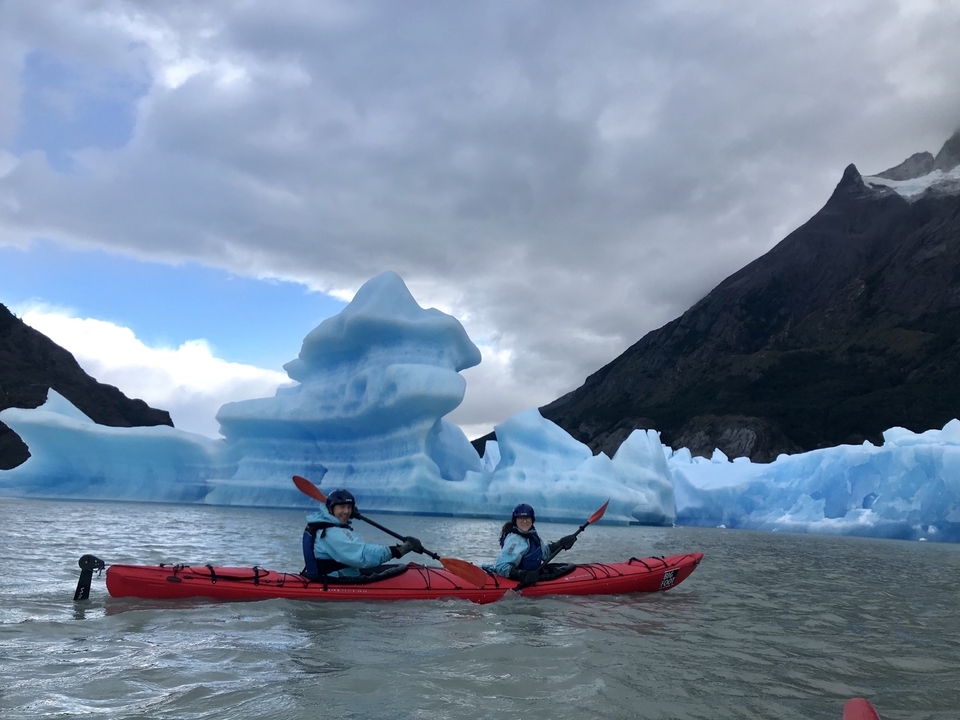 Des gens faisant du kayak parmi les icebergs avec des montagnes en arrière-plan.
