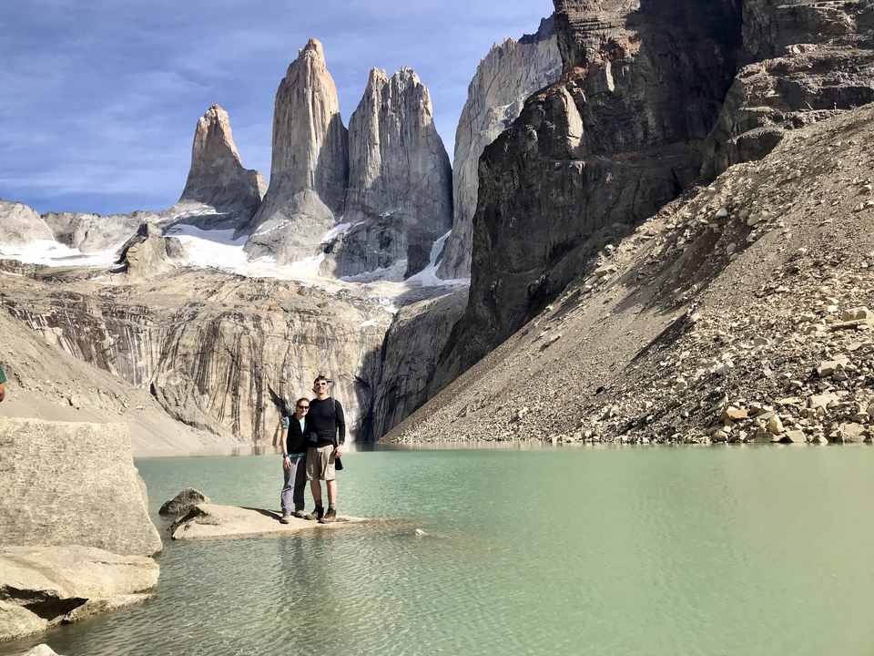 Deux personnes debout près d'un lac turquoise avec un paysage montagneux en arrière-plan.
