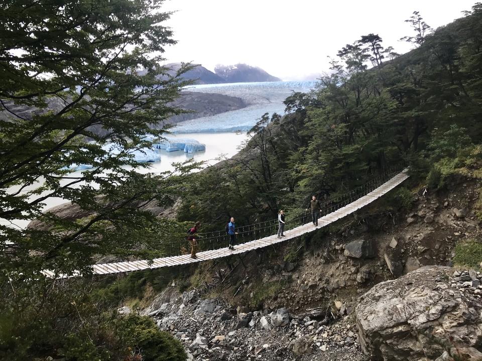 Des gens qui marchent sur un pont avec un glacier en arrière-plan.