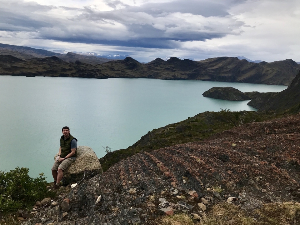 Personne assise sur un rocher au bord d'un lac avec un paysage montagneux en arrière-plan.