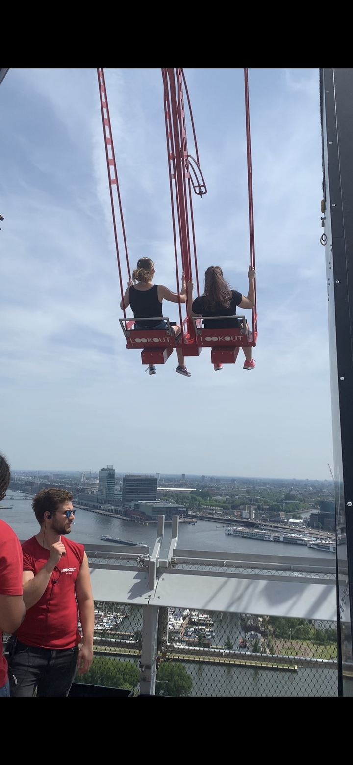 Deux personnes sur une attraction à bascule en hauteur avec l'horizon urbain en arrière-plan.