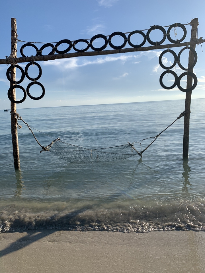 Hammock tied between two poles over water during sunset.