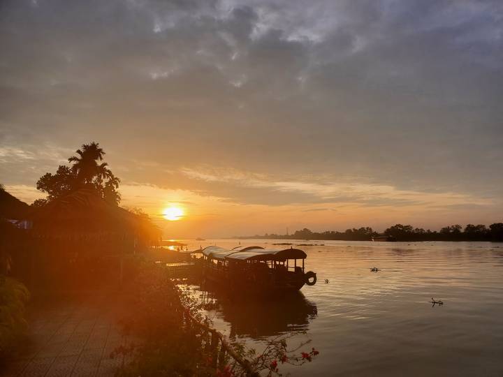 Coucher de soleil sur l'eau avec de petits bateaux et un environnement brumeux.