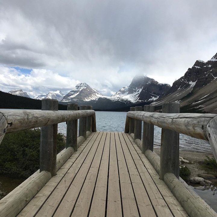 Wooden pier leading out to a lake with majestic mountains.