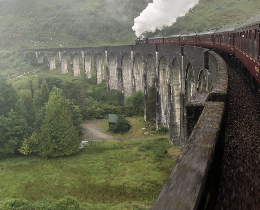 Train à vapeur traverse un viaduc en pierre emblématique dans une végétation luxuriante