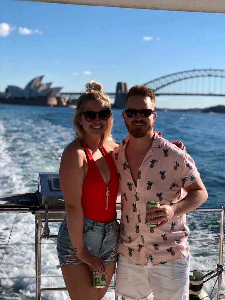 Deux personnes souriantes sur un bateau avec l'Opéra de Sydney en arrière-plan.