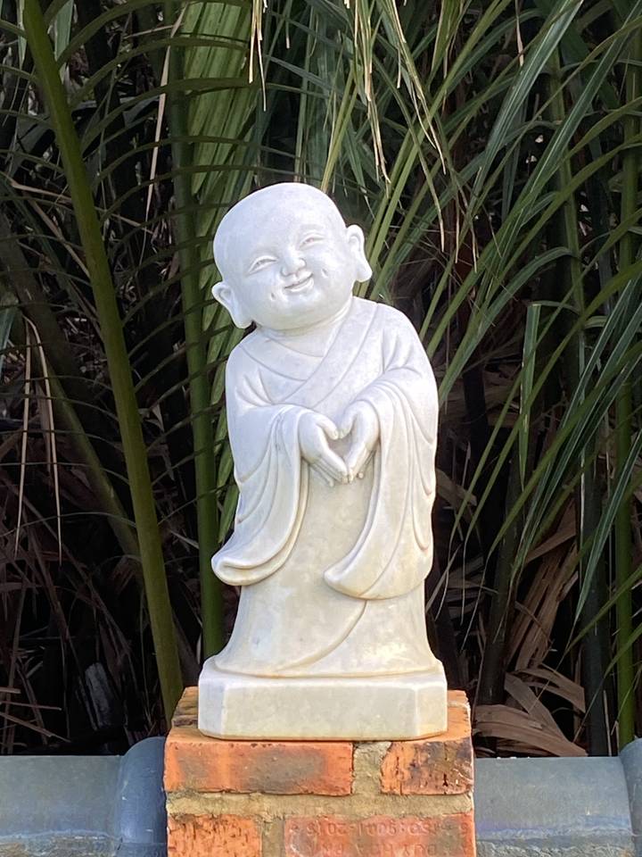 Statue de marbre d'une petite figure dans un cadre de jardin.