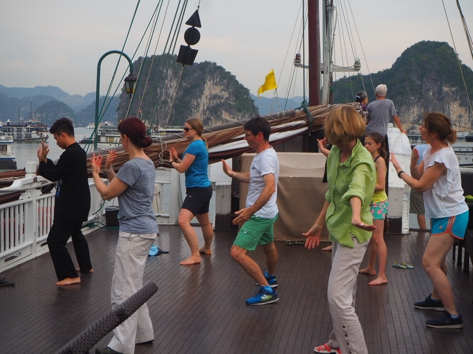 Groupe sur un bateau faisant de l'exercice ou dansant avec des falaises pittoresques en arrière-plan.