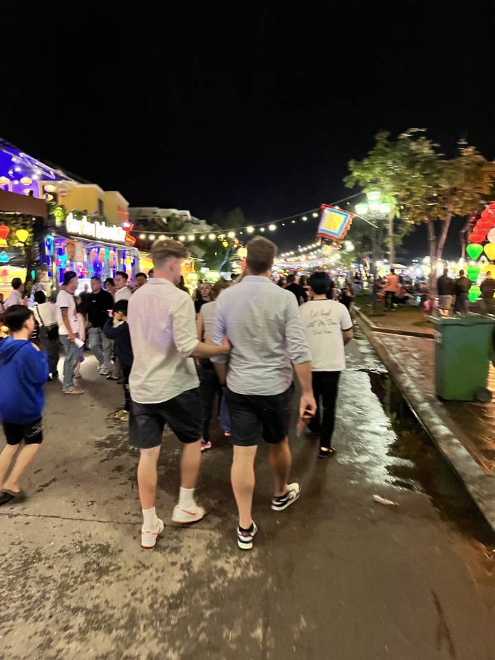 Des gens marchant dans une rue éclairée avec des magasins la nuit.