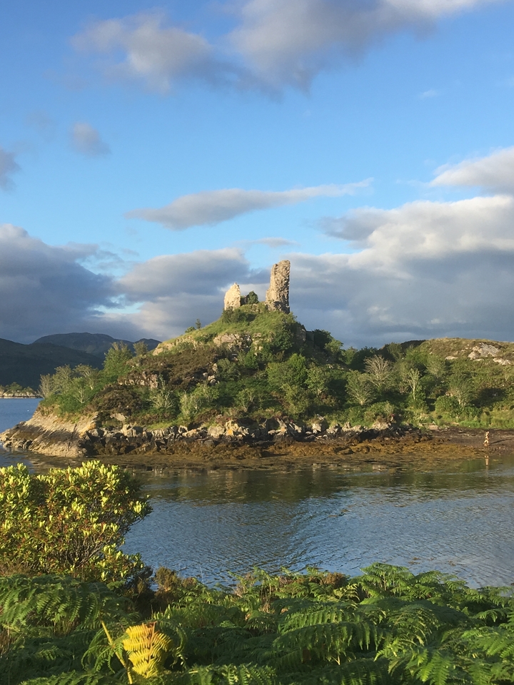 Ruins of a castle on a hill by a loch.