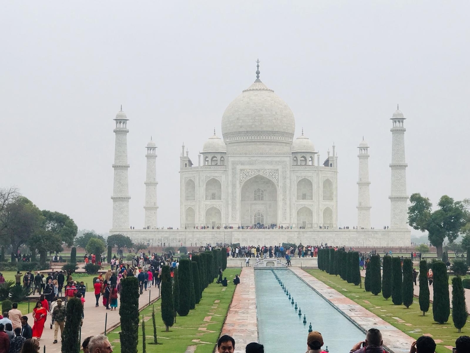 Vue lointaine du Taj Mahal avec les jardins environnants et les visiteurs.