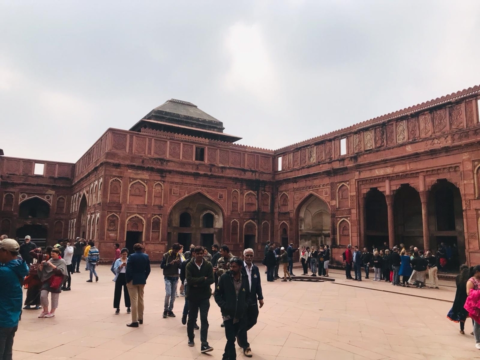 Des visiteurs dans une cour ouverte d'édifices en grès rouge.