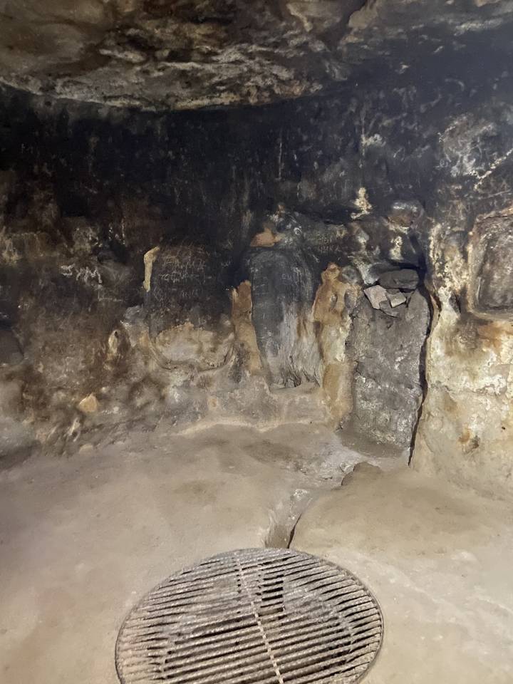 Intérieur de grotte sombre avec quelques graffitis et formations rocheuses.