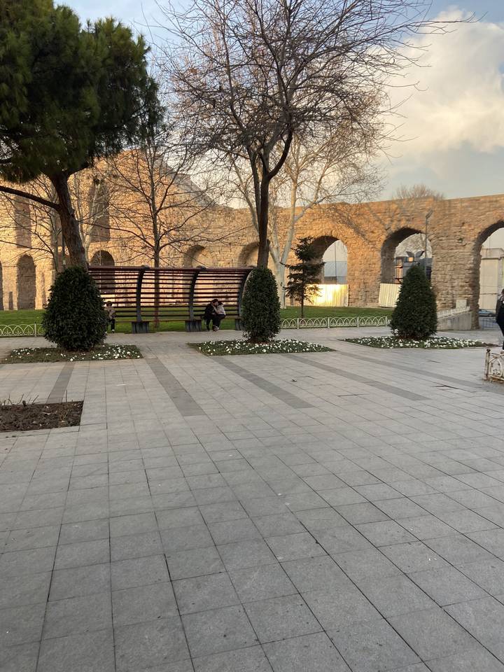 Ruines d'un aqueduc historique avec des arbres et des bancs.