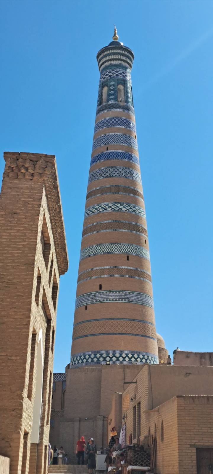 Grand minaret aux motifs complexes se détachant sur un ciel bleu dégagé.