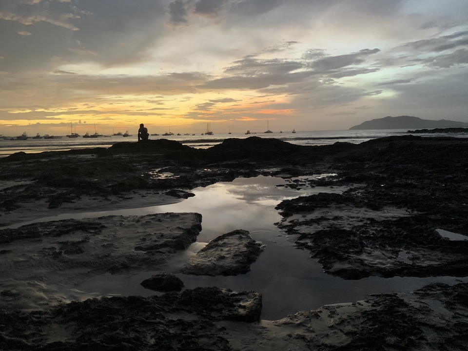 Plage rocheuse au coucher du soleil avec des bateaux à l'horizon.