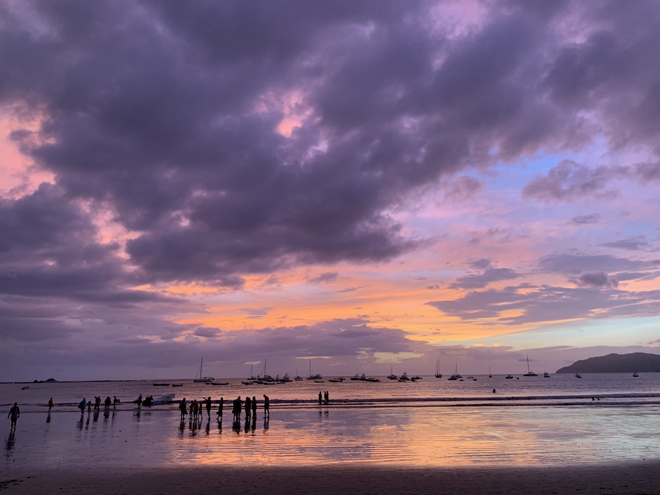 Silhouettes de personnes sur une plage avec un coucher de soleil coloré.