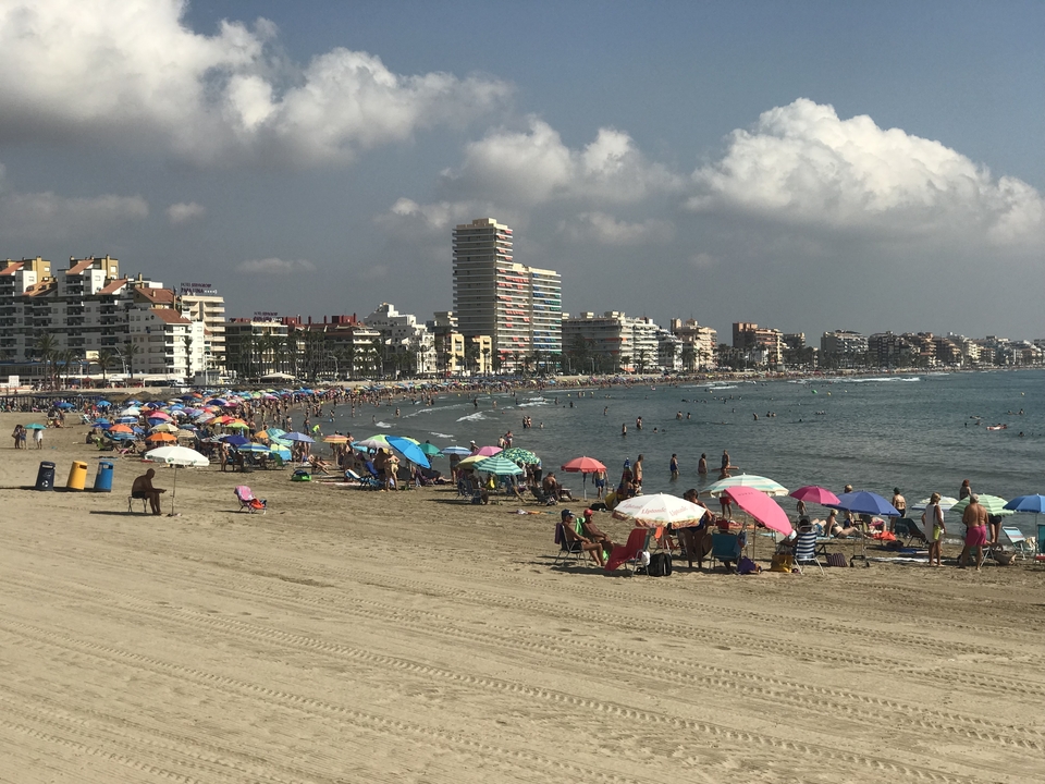 Plage bondée avec des parasols colorés et un paysage urbain en arrière-plan.