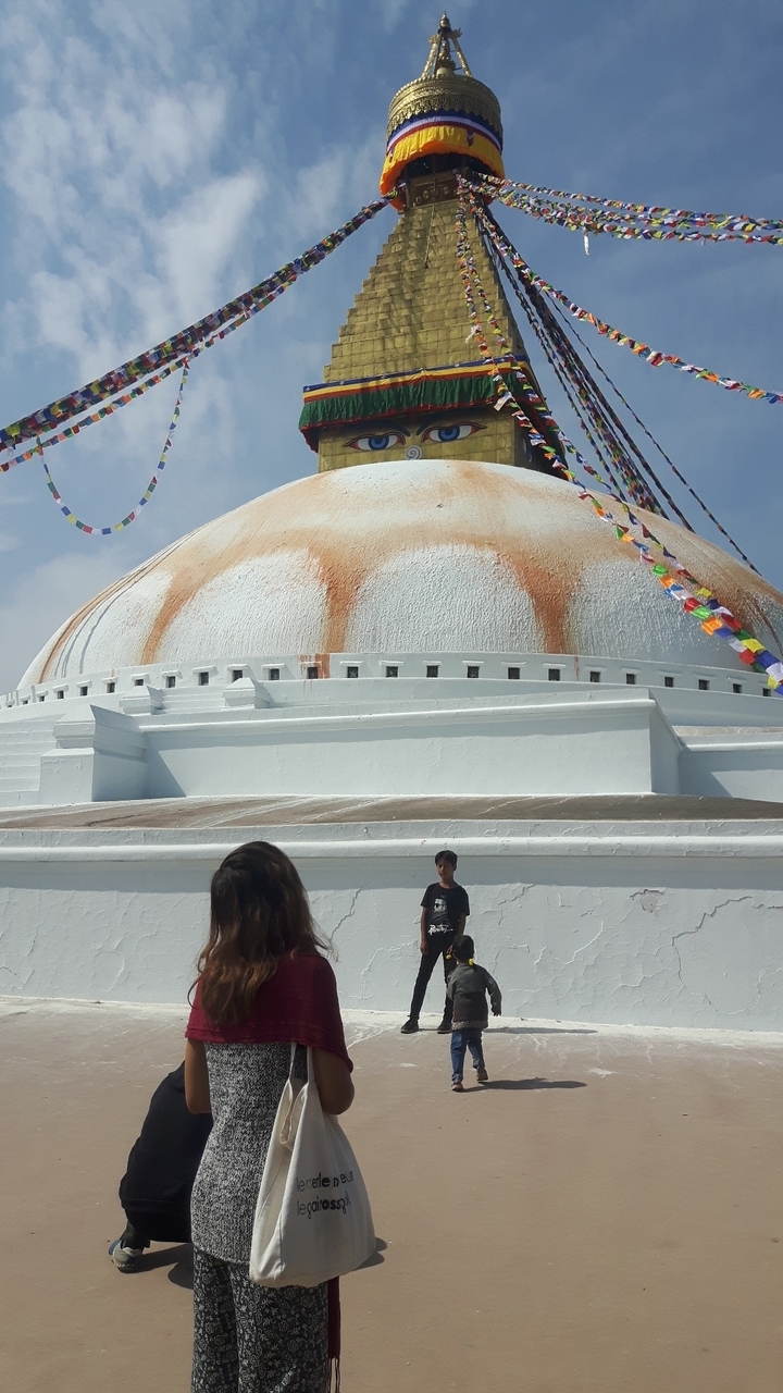 Grand stupa avec drapeaux de prière et des gens à la base.
