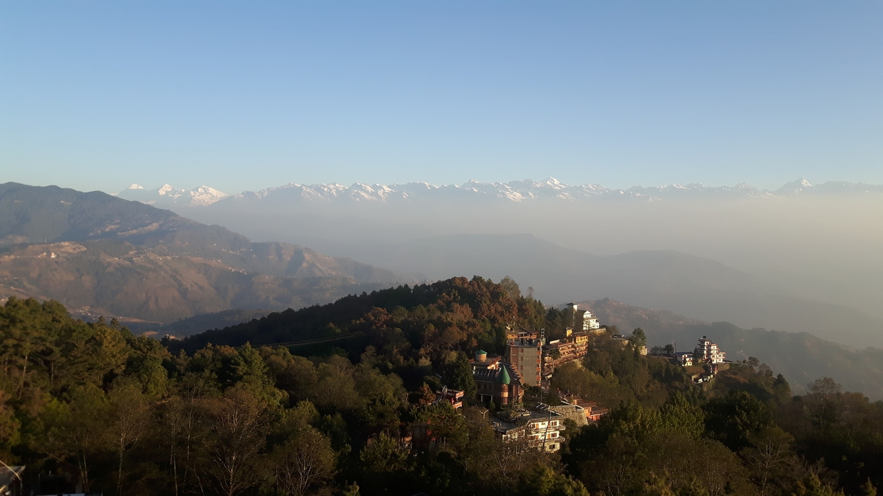Paysage montagneux avec une vue lointaine d'un village et un ciel dégagé.