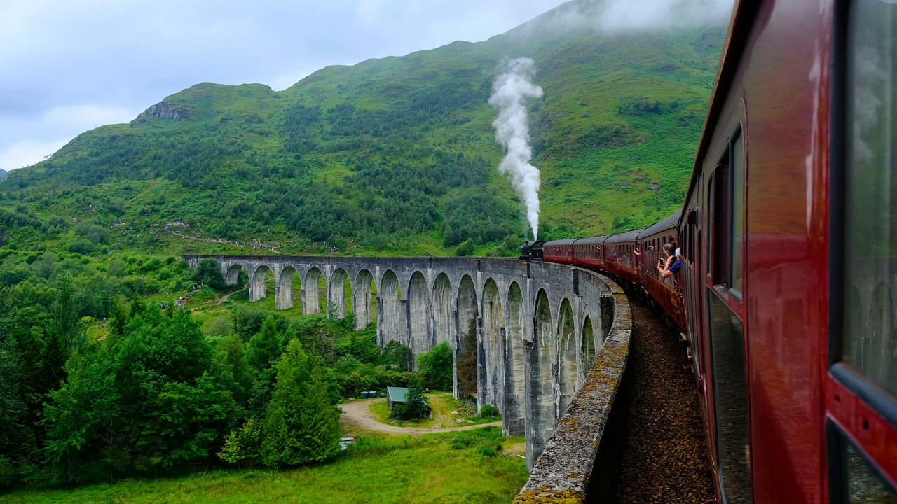 Train sur le viaduc de Glenfinnan avec une colline verdoyante luxuriante.