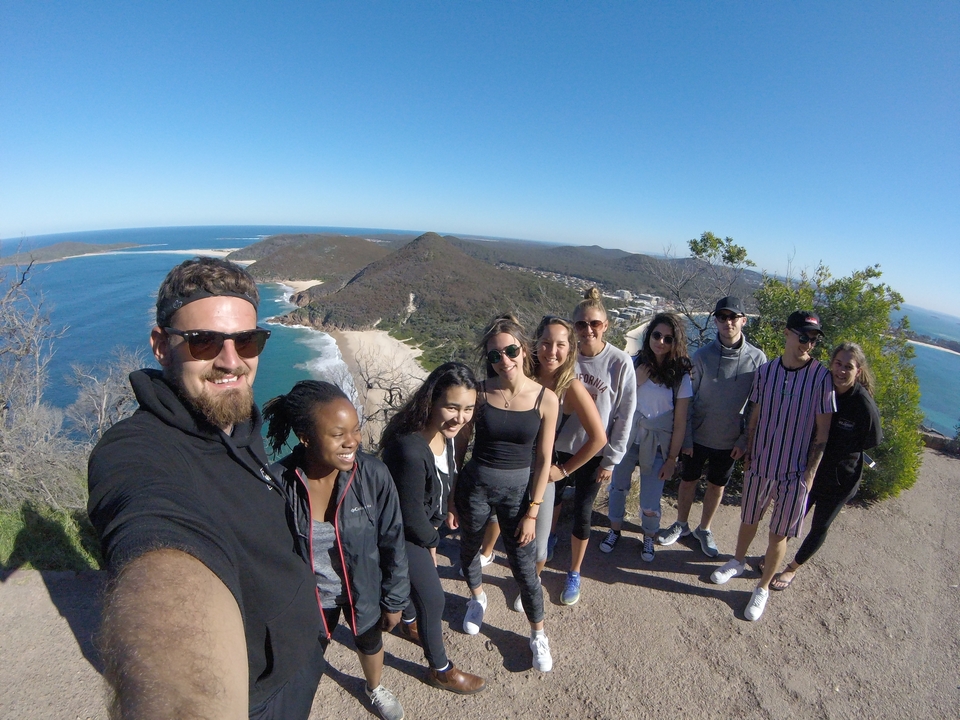 Group of people posing with a view of coastline and hills in the background.