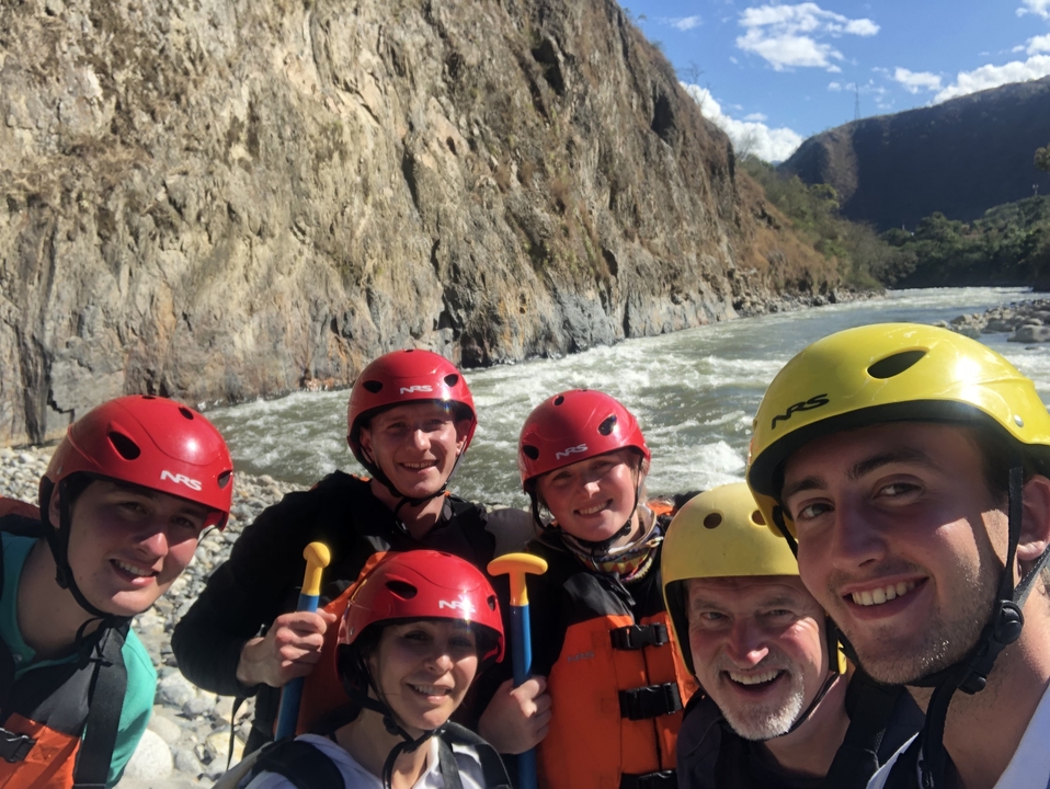 Groupe de personnes portant des casques posant près d'une rivière avec un arrière-plan rocheux.