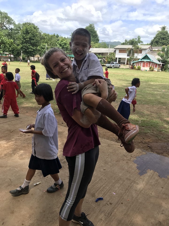 Femme jouant avec des enfants à l'extérieur dans une zone herbeuse.