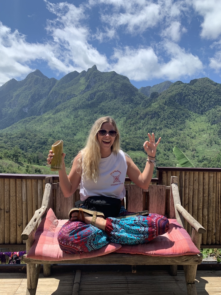 Femme tenant une tasse en bambou devant un paysage montagneux pittoresque.