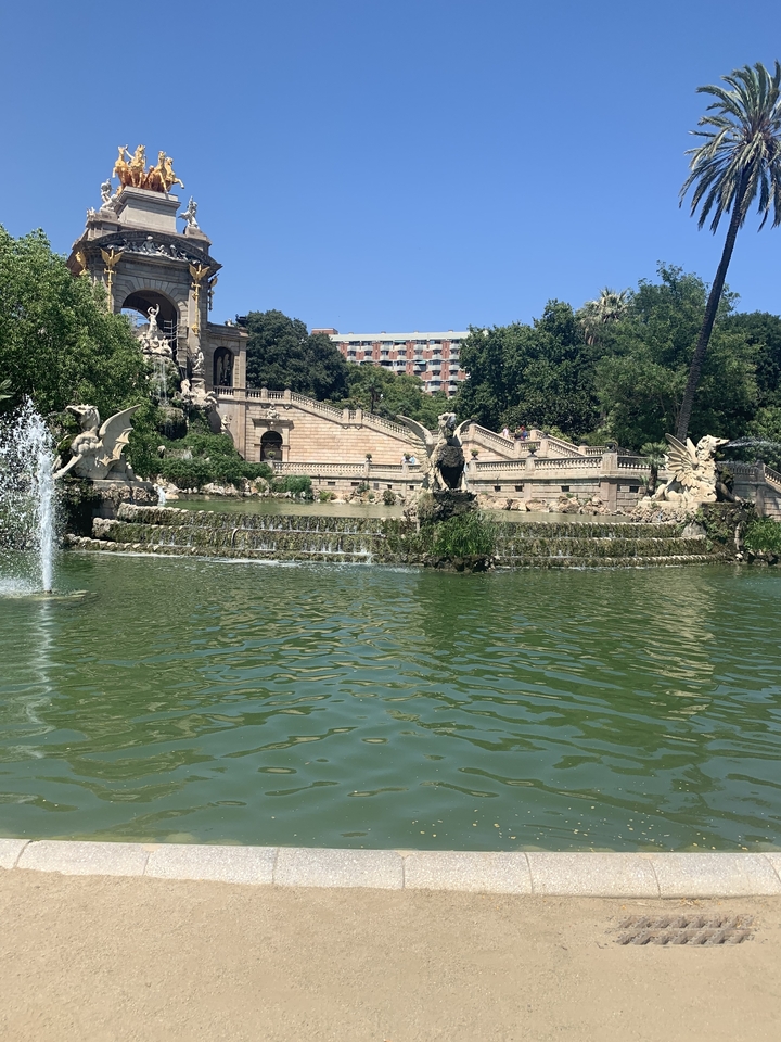 Fontaine ornée entourée de verdure avec des marches menant au loin.