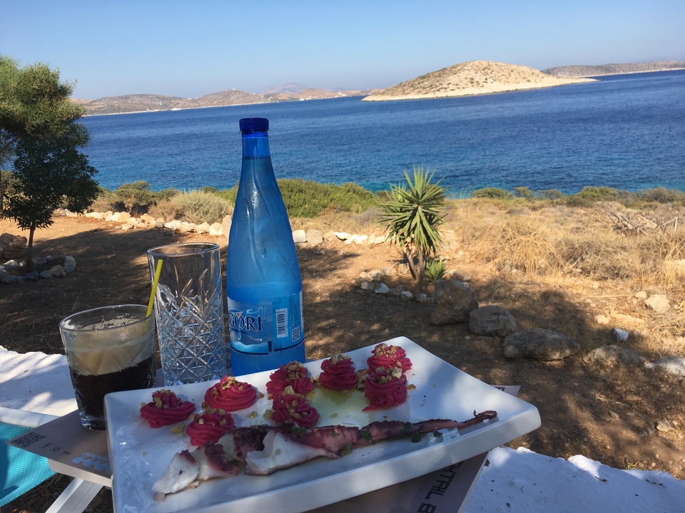 Table avec des plats et une bouteille au bord de la mer avec une île en arrière-plan.