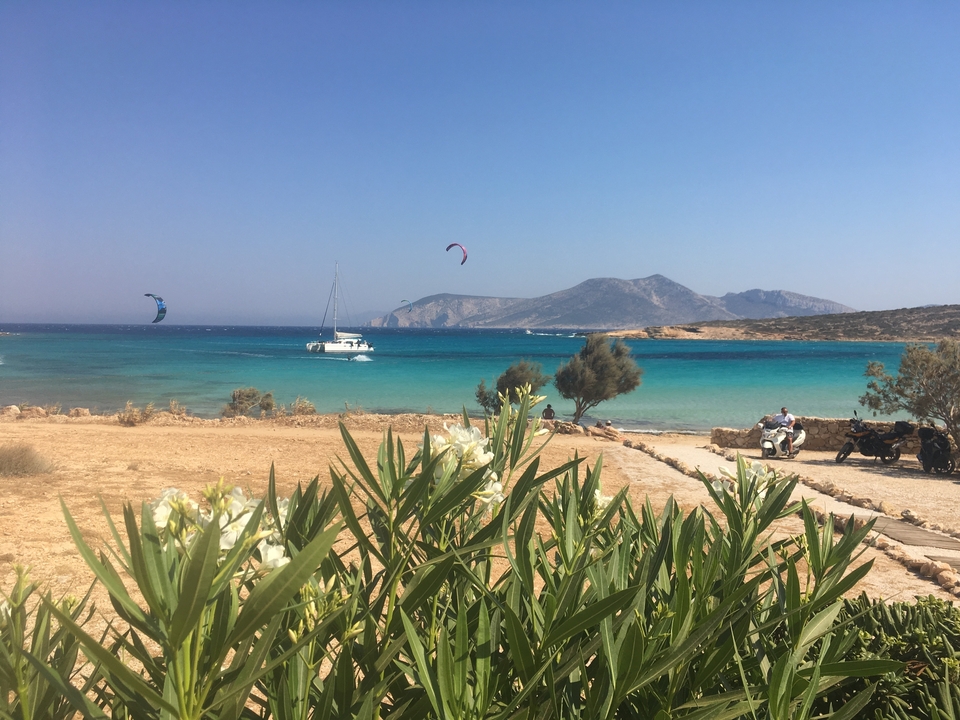 Kitesurf et voile dans une mer turquoise éclatante avec des montagnes en arrière-plan.