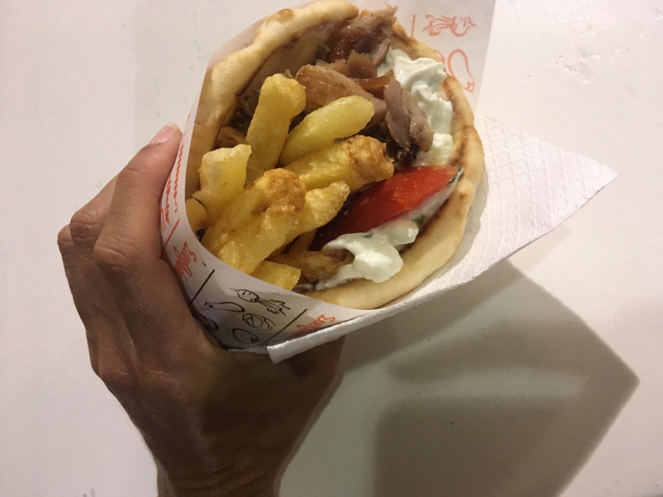 Main tenant un gyro avec des frites et de la sauce tzatziki.