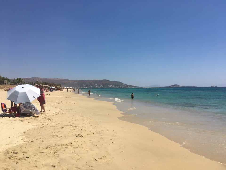 Plage de sable avec des gens qui profitent de l'eau et des parasols pour l'ombre.