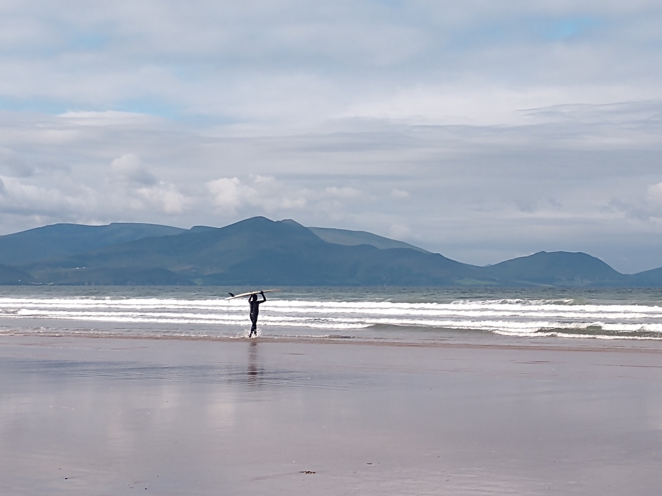 Personne portant une planche de surf par une journée nuageuse sur la plage.
