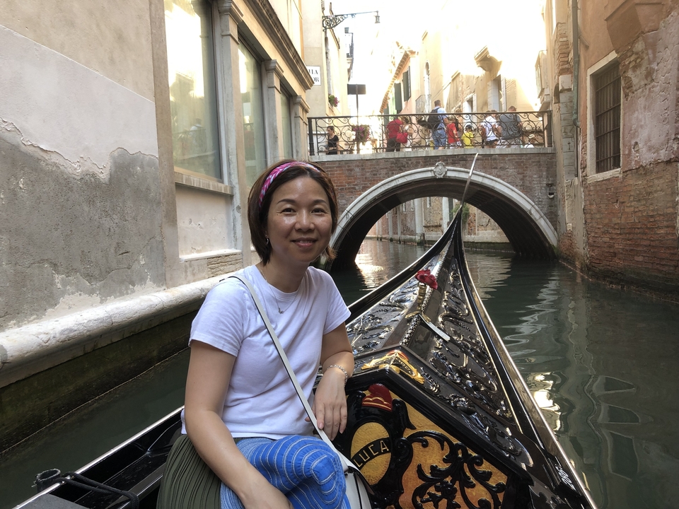 Une personne souriante lors d'une promenade en gondole à travers un canal étroit avec un pont au-dessus.