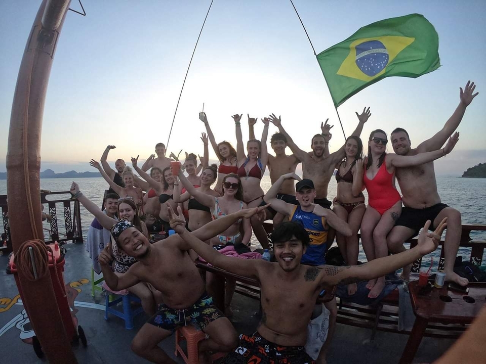 Group of people celebrating on a boat with a Brazilian flag at sunset.