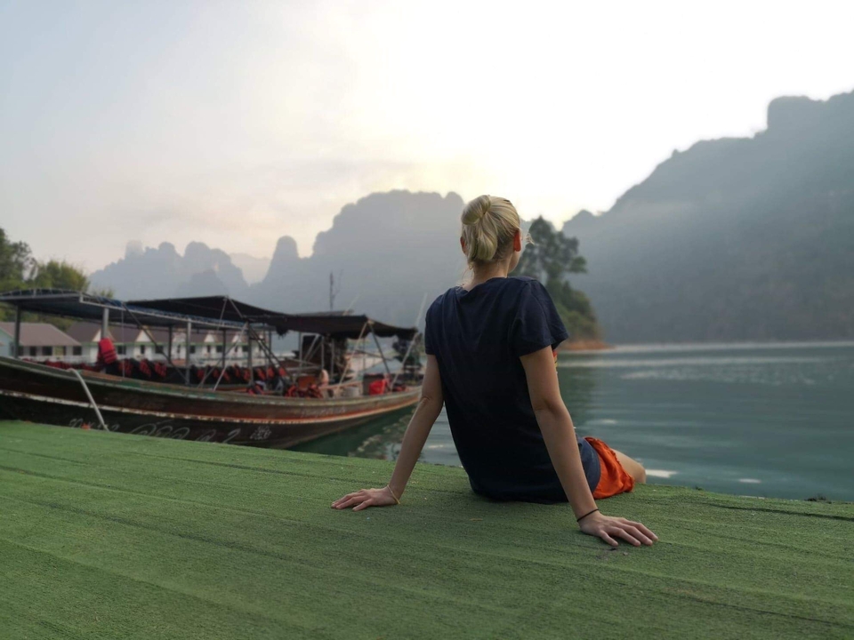 Person sitting on a pier looking over the water with a boat nearby.