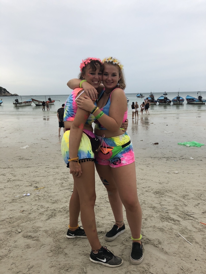 Two friends posing on a beach with boats and water in the background.
