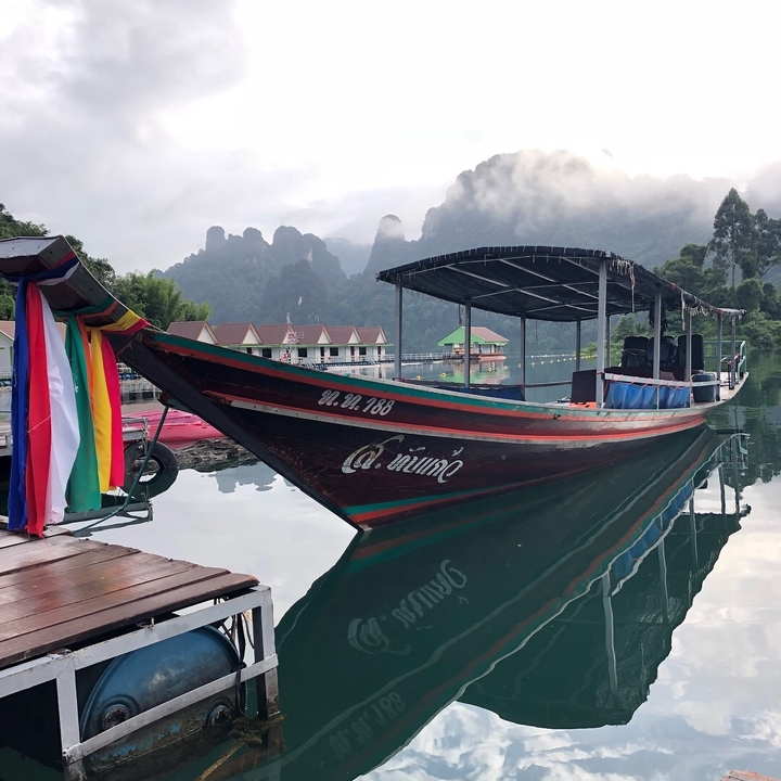 Longtail boat docked in calm water with mountains in the background.