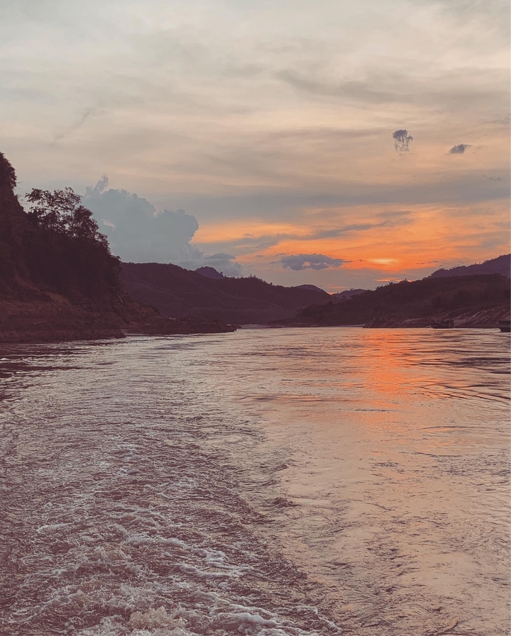 Coucher de soleil serein sur une rivière avec des montagnes en silhouette.