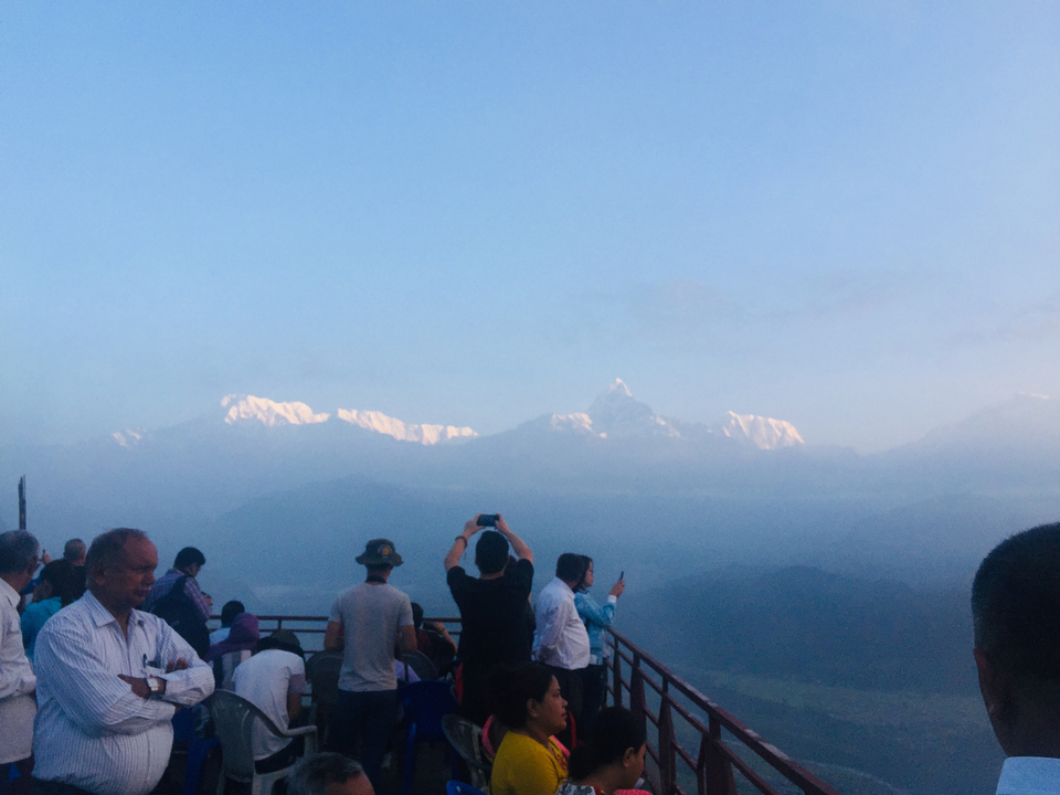Groupe de personnes sur une terrasse photographiant des montagnes enneigées.