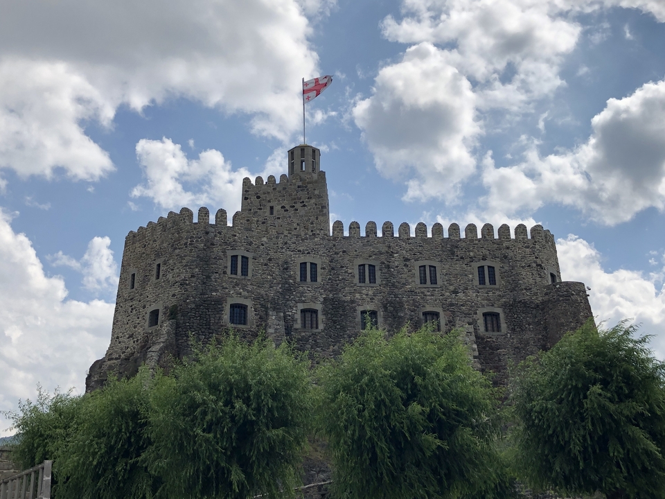 Une forteresse avec un drapeau géorgien au sommet sous un ciel nuageux.